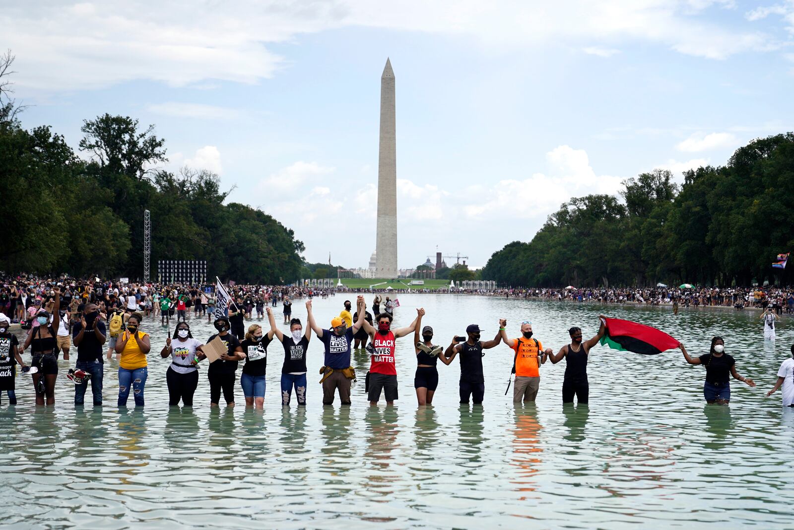 FILE - In this Friday, Aug. 28, 2020, file photo, people join hands as they pose for a photo in the Reflecting Pool in the shadow of the Washington Monument as they attend the March on Washington, at the Lincoln Memorial in Washington, on the 57th anniversary of the Rev. Martin Luther King Jr.'s "I Have A Dream" speech. California lawmakers are setting up a task force to study and make recommendations for reparations to African-Americans, particularly the descendants of slaves, as the nation struggles again with civil rights and unrest following the latest shooting of a Black man by police. The state Senate supported creating the nine-member commission on a bipartisan 33-3 vote Saturday, Aug. 29, 2020. (AP Photo/Julio Cortez, File)