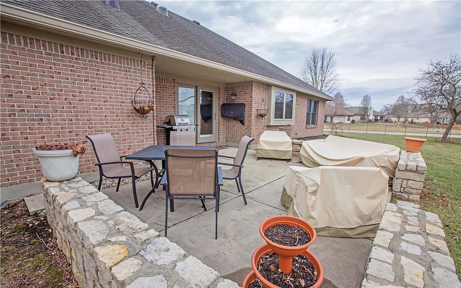 The rear of the home has a concrete patio with a portion that is covered. It overlooks a lake beyond the fence.