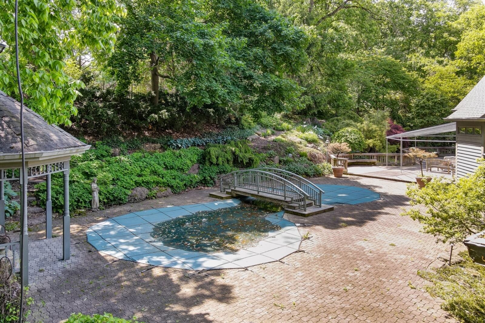 The backyard includes an in-ground swimming pool with bridge, a spacious paver-brick patio and a large wooden deck with awnings.