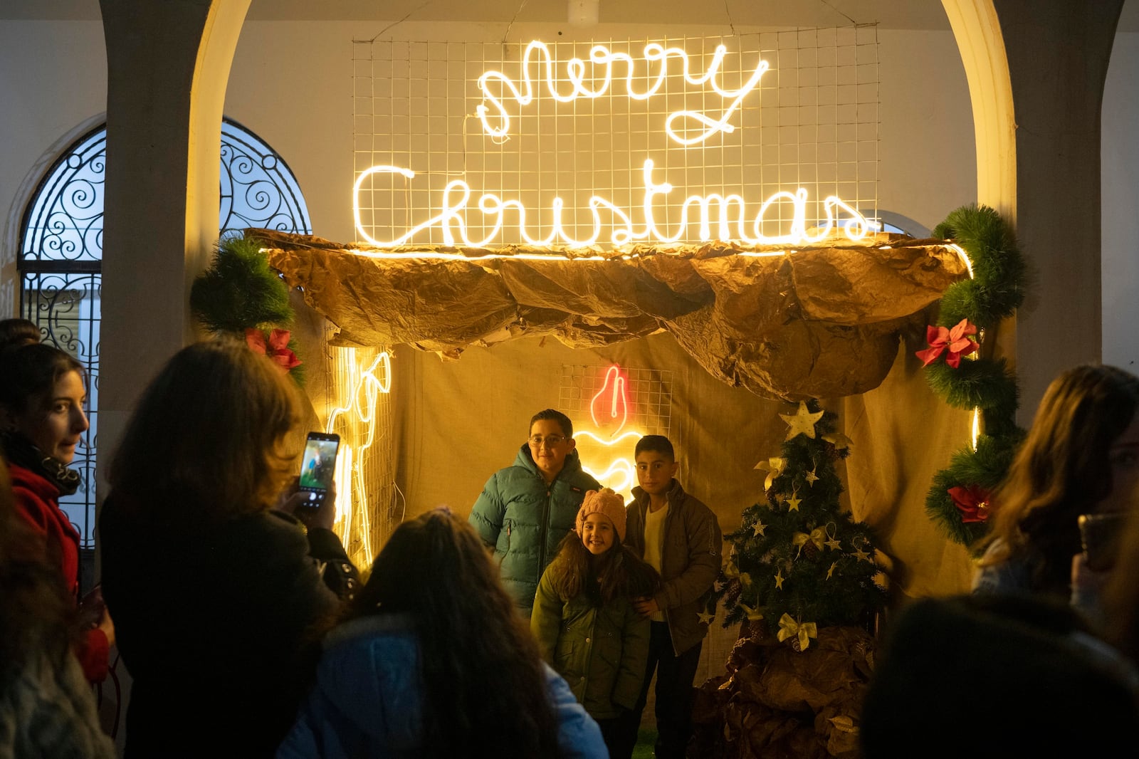 People pose for the photo next to Christmas decoration after attending a Christmas mass at the church of St. George, in Maaloula, some 60 km northern Damascus, Syria, Tuesday, Dec. 24, 2024. (AP Photo/Leo Correa)