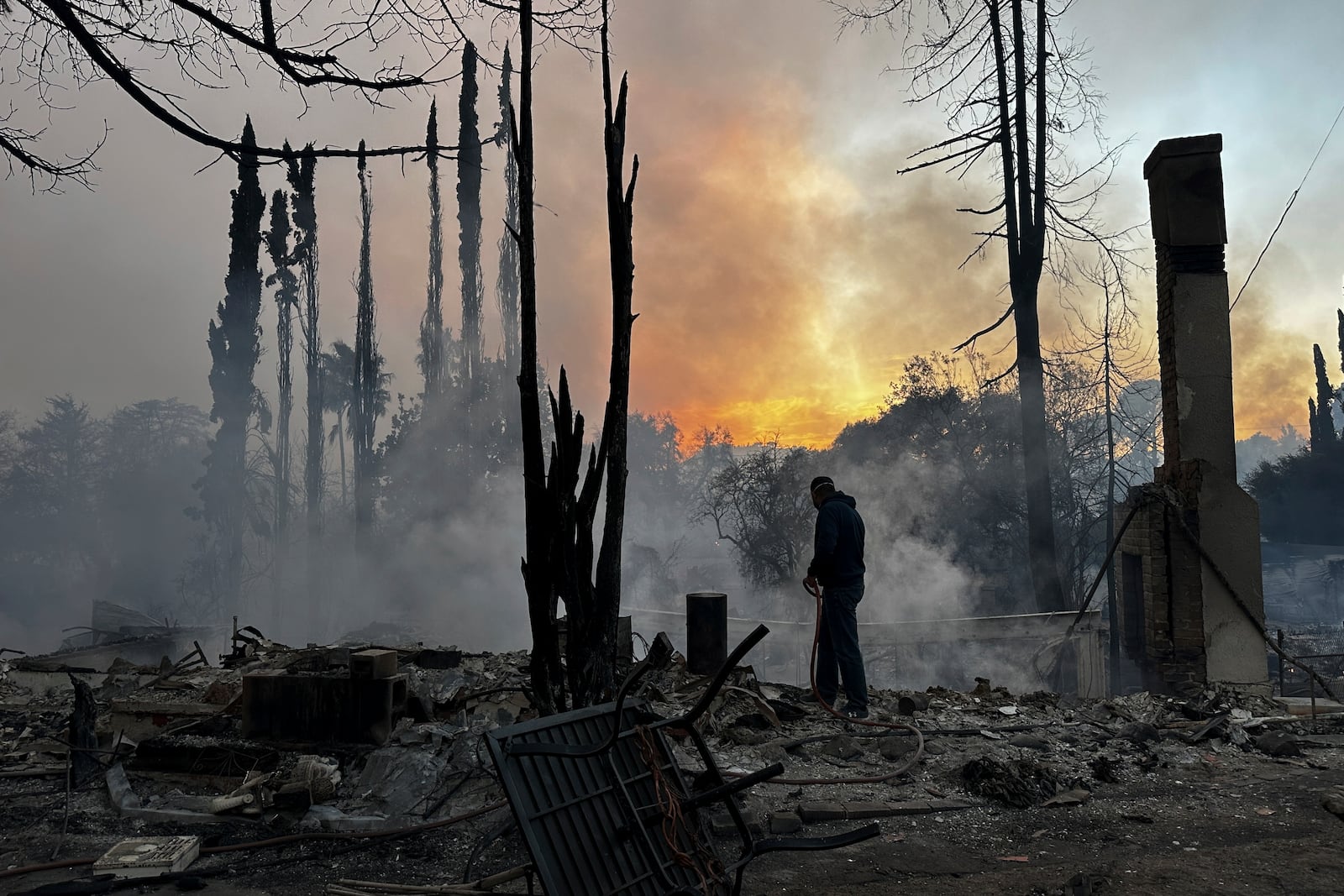 A resident hoses down hot spots in a fire-ravaged property after the Palisades Fire swept through in the Pacific Palisades neighborhood of Los Angeles, Wednesday, Jan. 8, 2025. (AP Photo/Eugene Garcia)