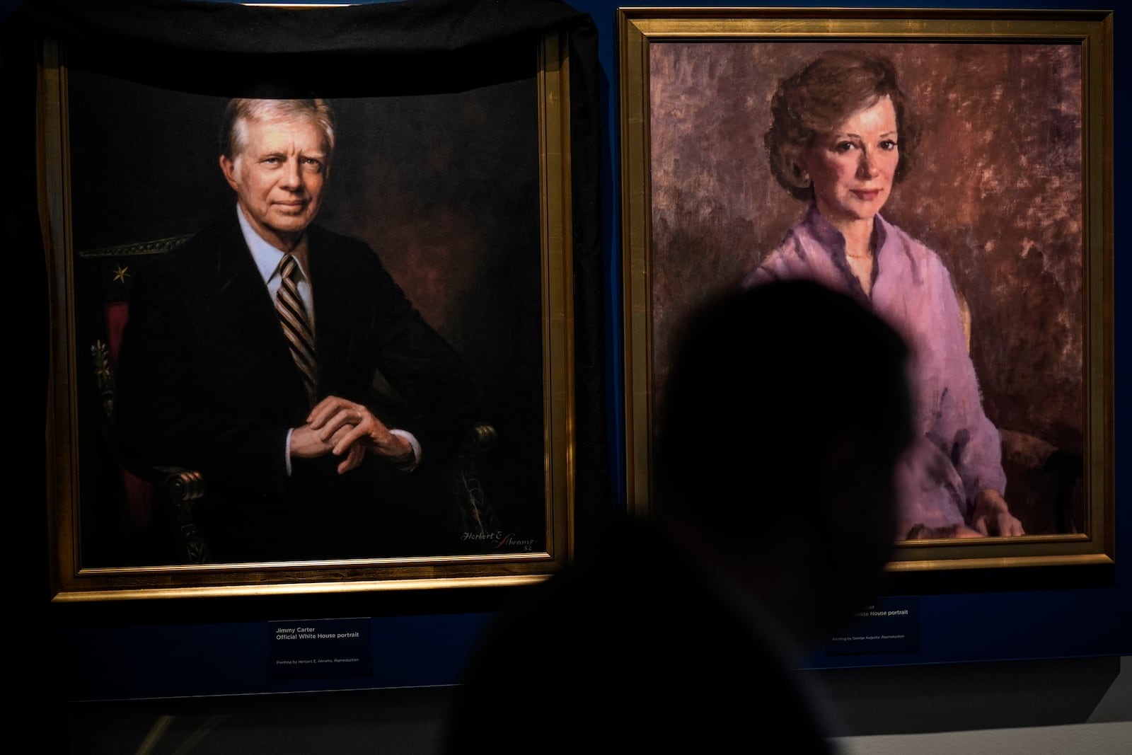 A man moves by the portrait of former President Jimmy Carter and his wife Rosalynn Carter at the Jimmy Carter National Historical Park, Monday, Dec. 30, 2024, in Plains, Ga. Jimmy Carter died Sunday at the age of 100. (AP Photo/Mike Stewart)