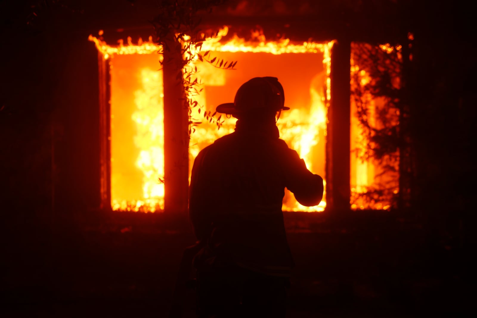 A firefighter is silhouetted in front of a burning structure as the Palisades Fire sweeps through in the Pacific Palisades neighborhood of Los Angeles, Tuesday, Jan. 7, 2025. (AP Photo/Etienne Laurent)