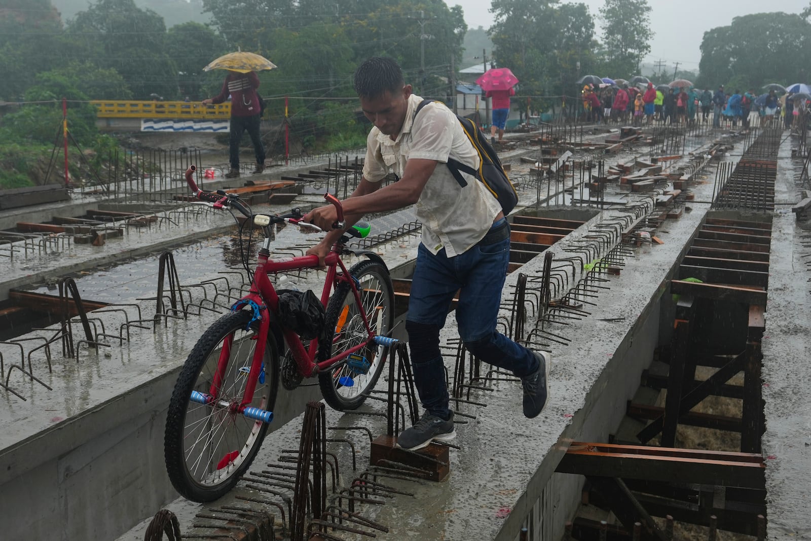 Residents cross a bridge under construction amid rain showers brought on by Tropical Storm Sara, on the outskirts of San Pedro Sula, Honduras, Saturday, Nov. 16, 2024. (AP Photo/Moises Castillo)