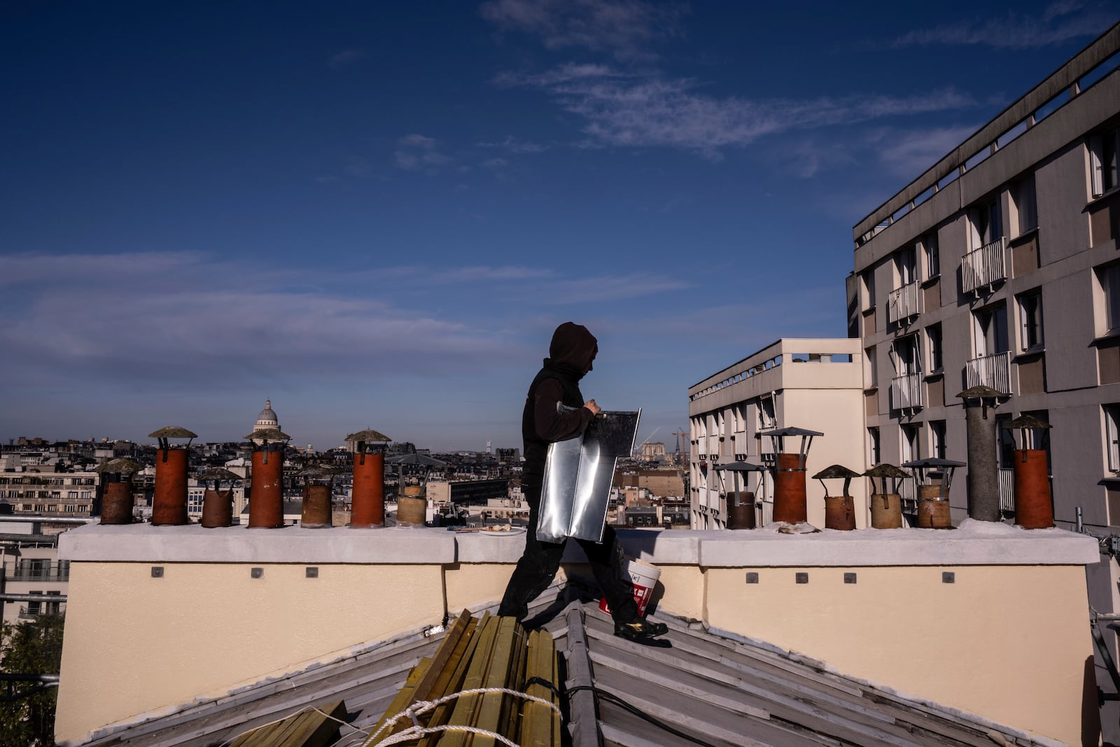 A roofer carries zinc sheets of a building in Paris, Wednesday, Nov. 20, 2024. (AP Photo/Louise Delmotte)