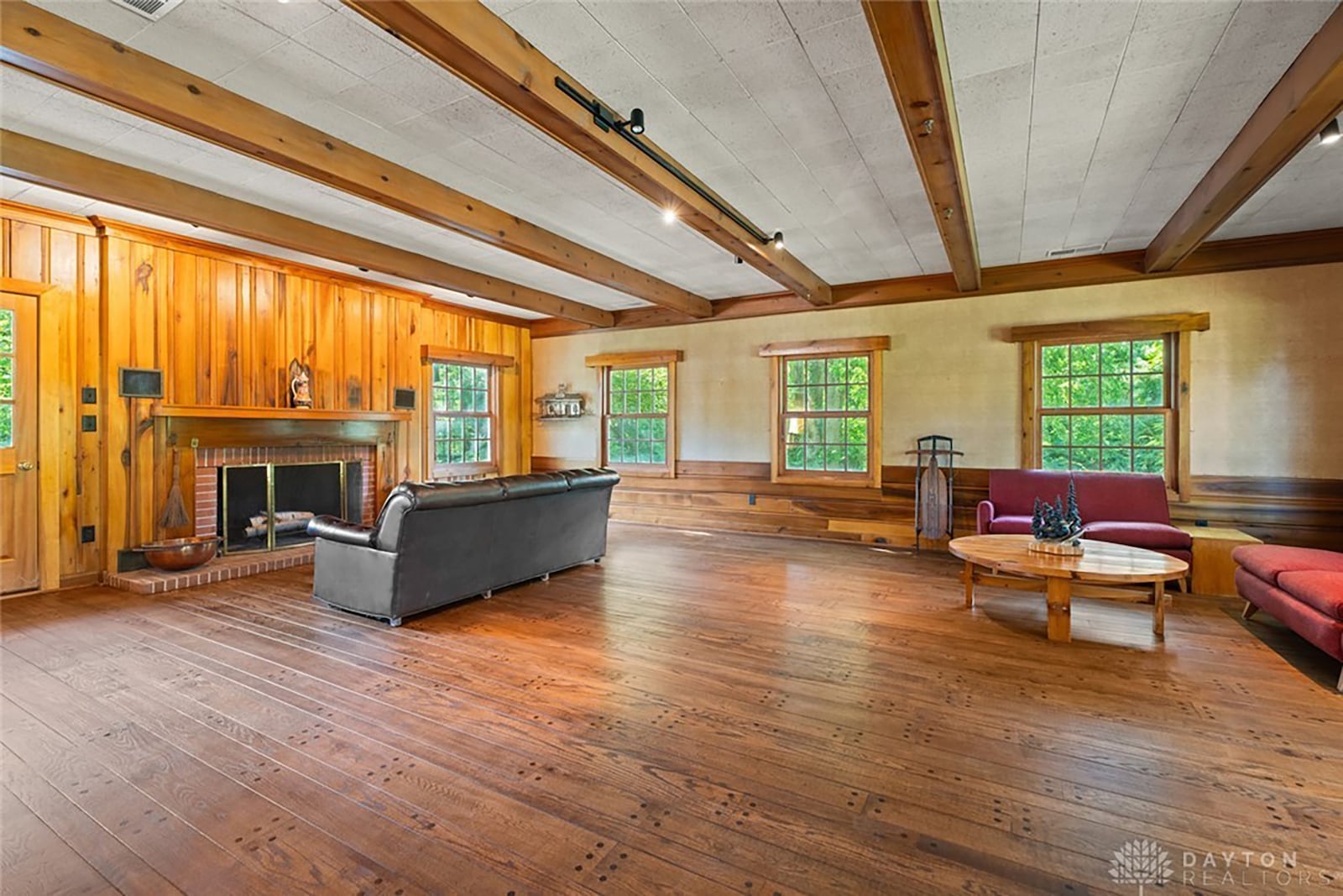 The lodge style family room on the main level has a woodburning fireplace, wood beams on the ceiling and wood paneling as well as wide plank style oak flooring.