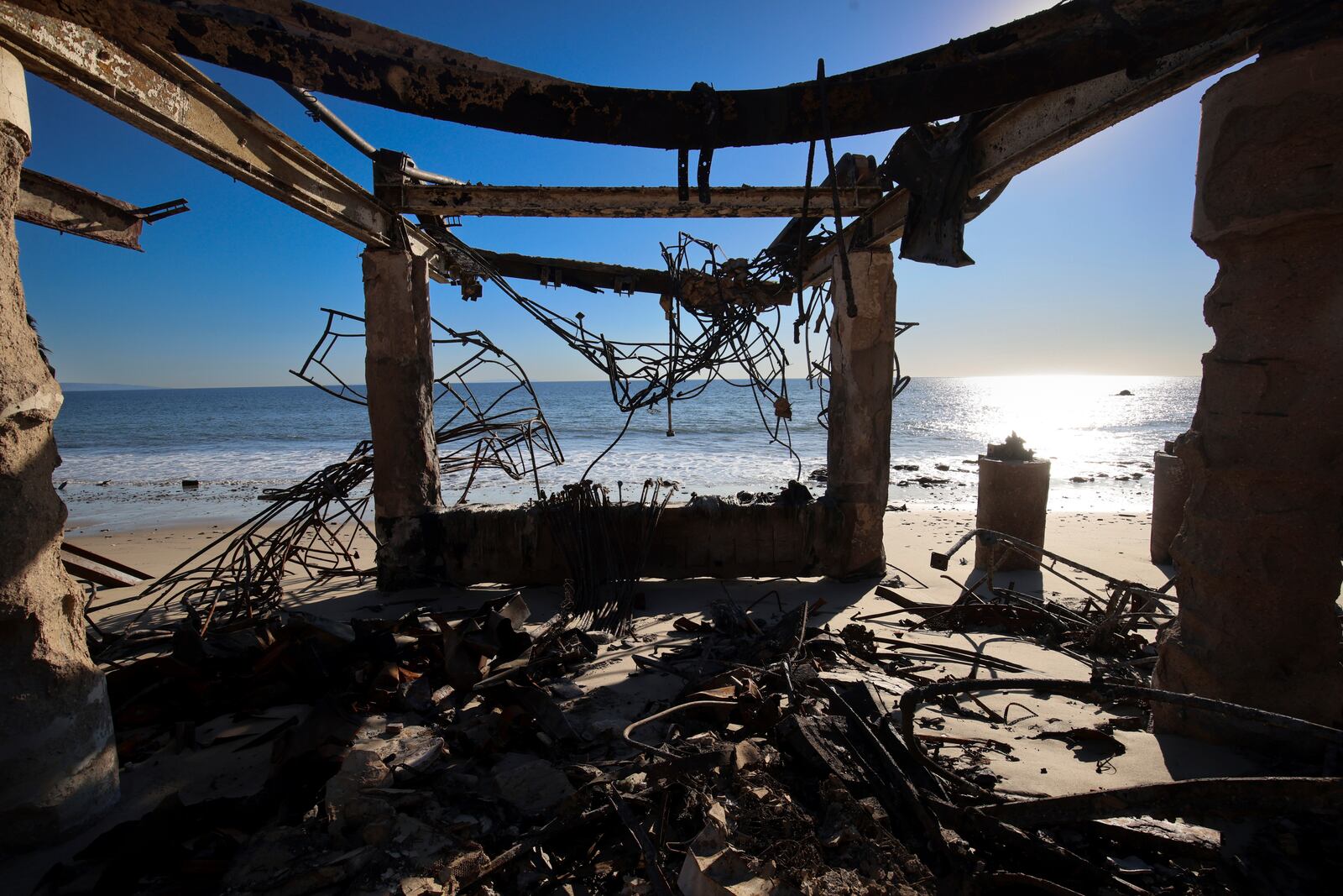 The Pacific Ocean is seen through a fire-ravaged property in the aftermath of the Palisades Fire Tuesday, Jan. 14, 2025 in Malibu, Calif. (AP Photo/Ethan Swope)