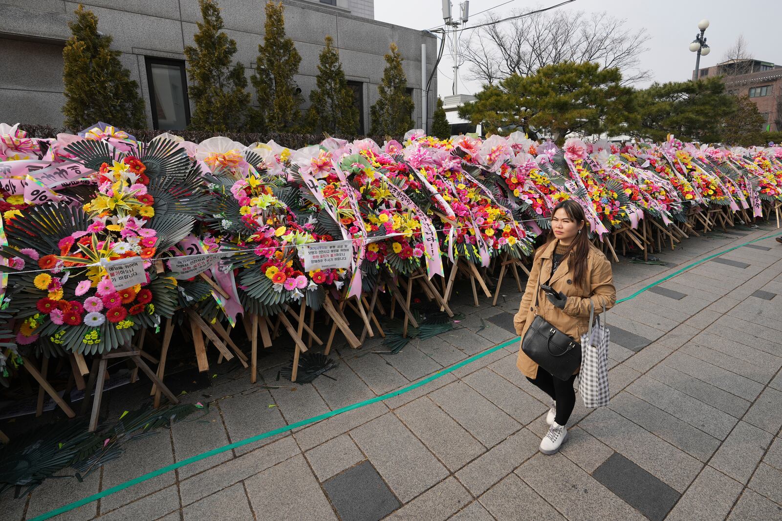 A pedestrian passes by the wreaths sent by supporters of impeached South Korean President Yoon Suk Yeol outside of the Constitutional Court in Seoul, South Korea, Tuesday, Jan. 14, 2025. (AP Photo/Lee Jin-man)