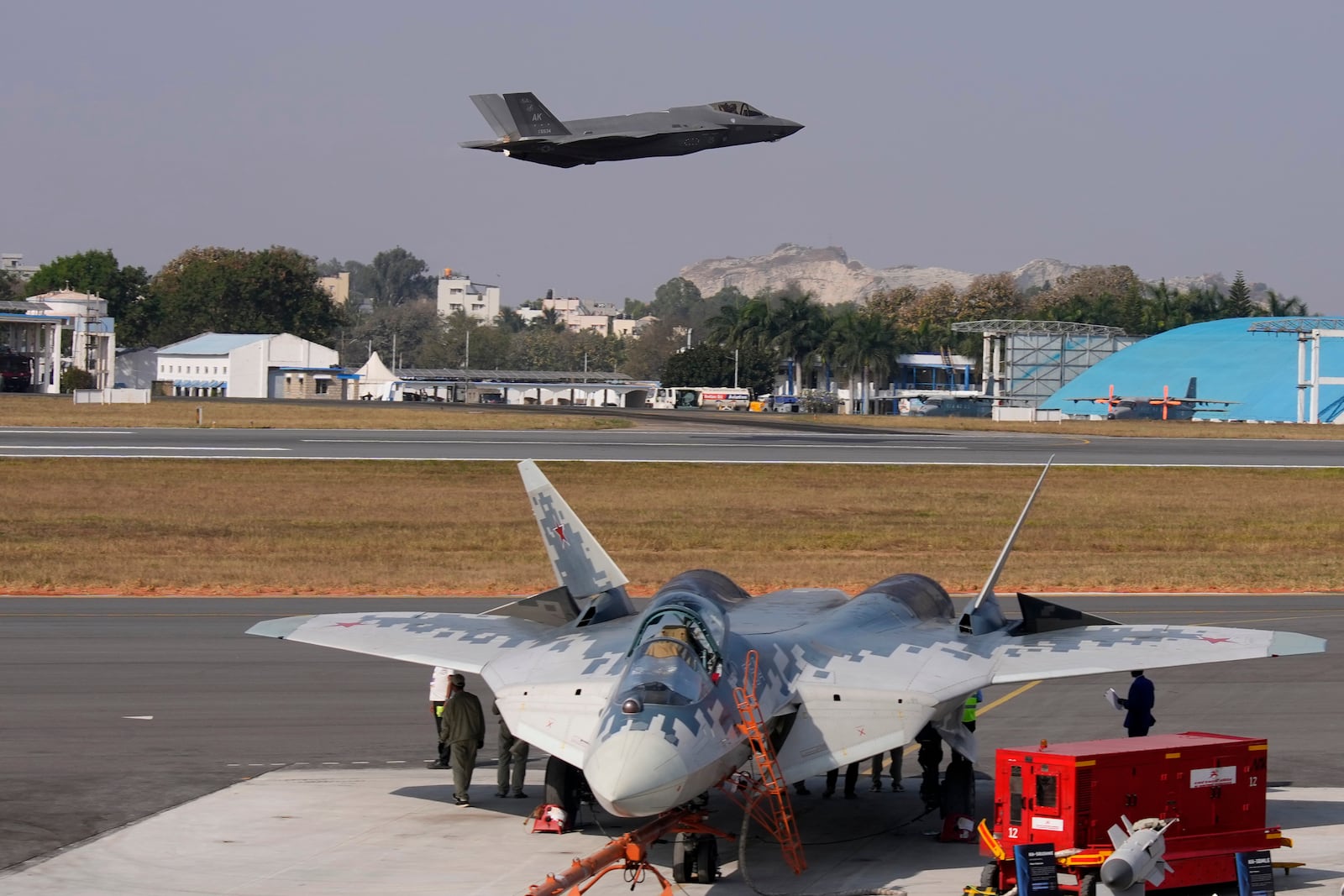 U.S. Air Force fighter aircraft F-35 flies over Russia's Su-57 fighter aircraft, parked at the static display area, on the fourth day of the Aero India 2025, a biennial event, at Yelahanka air base in Bengaluru, India, Thursday, Feb. 13, 2025. (AP Photo/Aijaz Rahi)