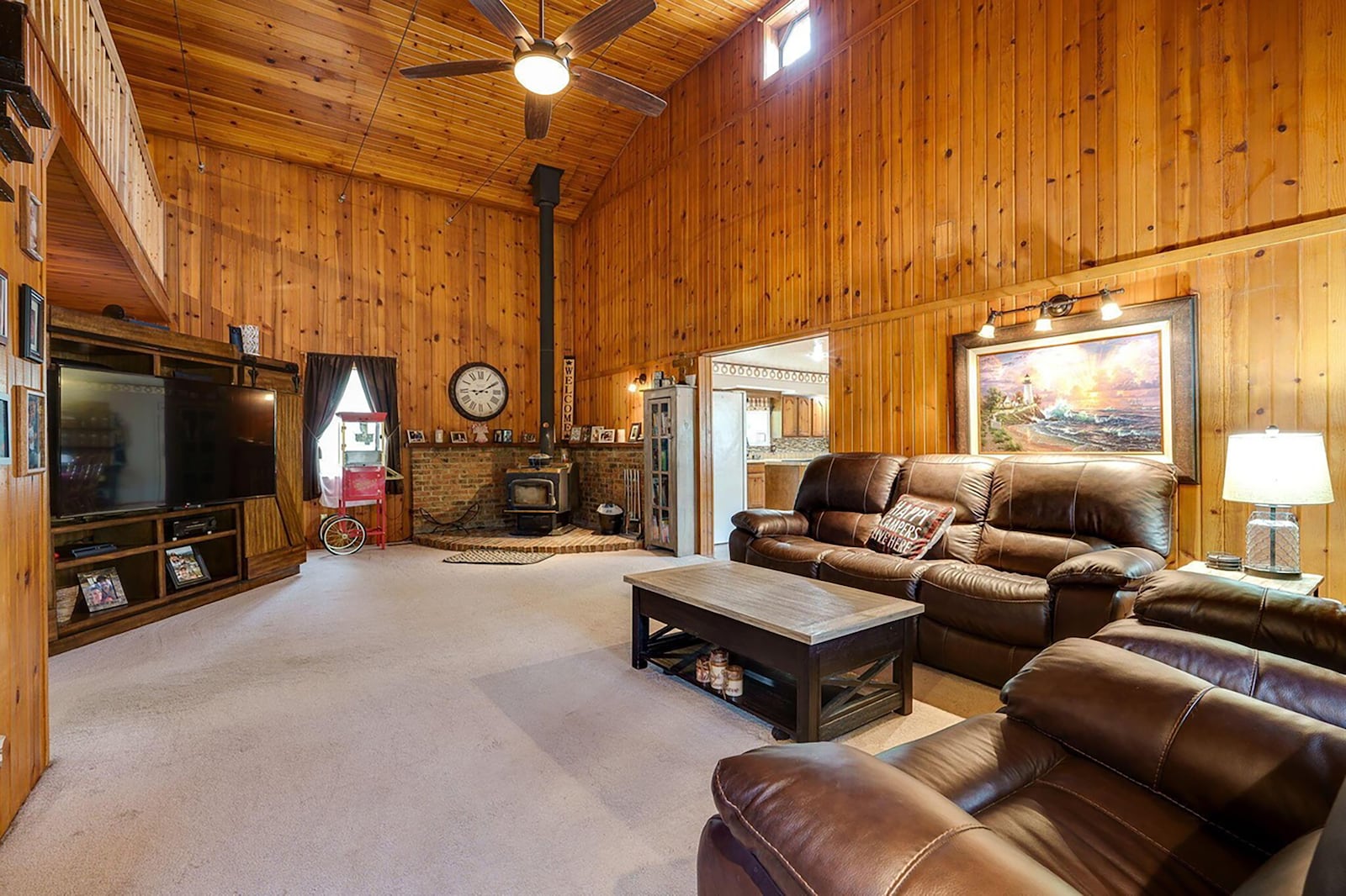 The two story living room was designed with a log cabin in mind. It has paneled walls and ceiling, a ceiling fan and a woodburning stove.