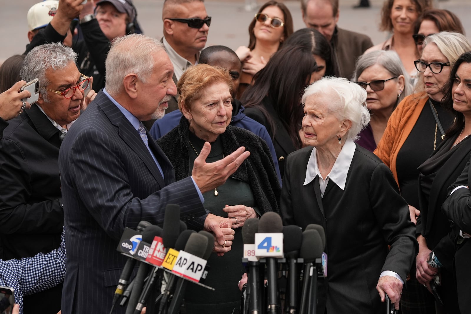 Holding the hand of Marta Cano, the sister of Jose Menendez, attorney Mark Geragos, left, talks to Joan VanderMolen, Erik and Lyle Menendez's aunt, during a news conference after a hearing in Los Angeles, Monday, Nov. 25, 2024. (AP Photo/Jae C. Hong)