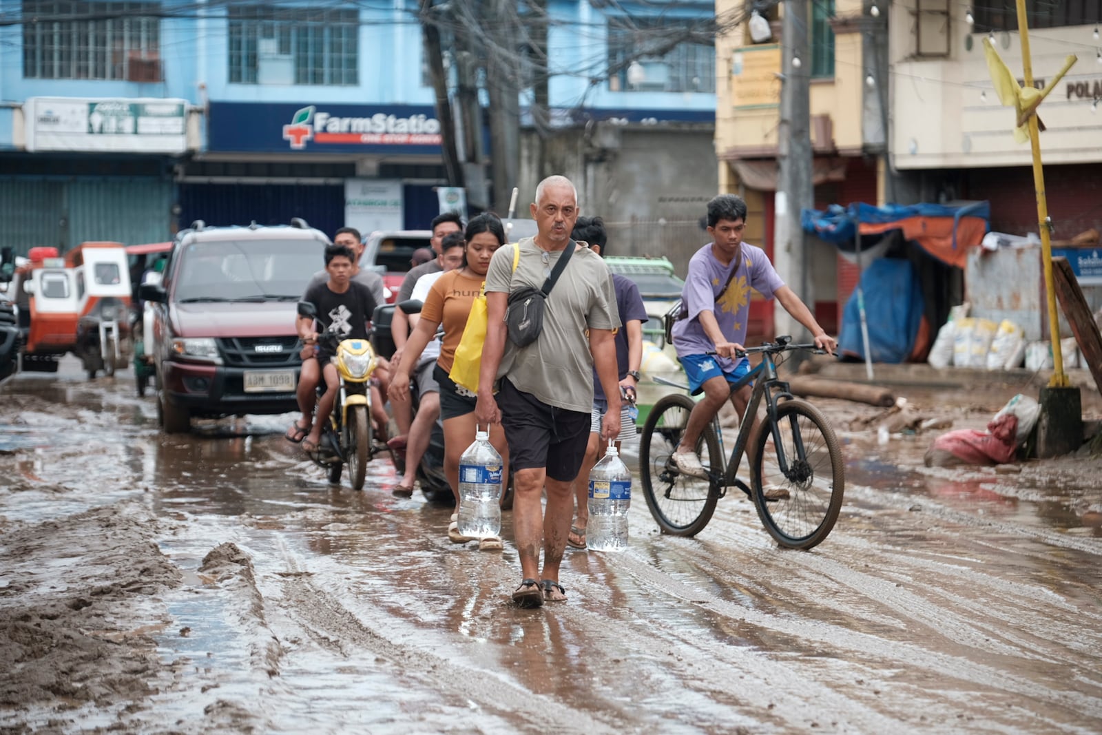 Residents walk along a muddied road as they start cleaning their area after floods caused by Tropical Trami, locally named Kristine, in Polangui, Albay province, Philippines on Oct. 23, 2024. (AP Photo/John Michael Magdasoc)