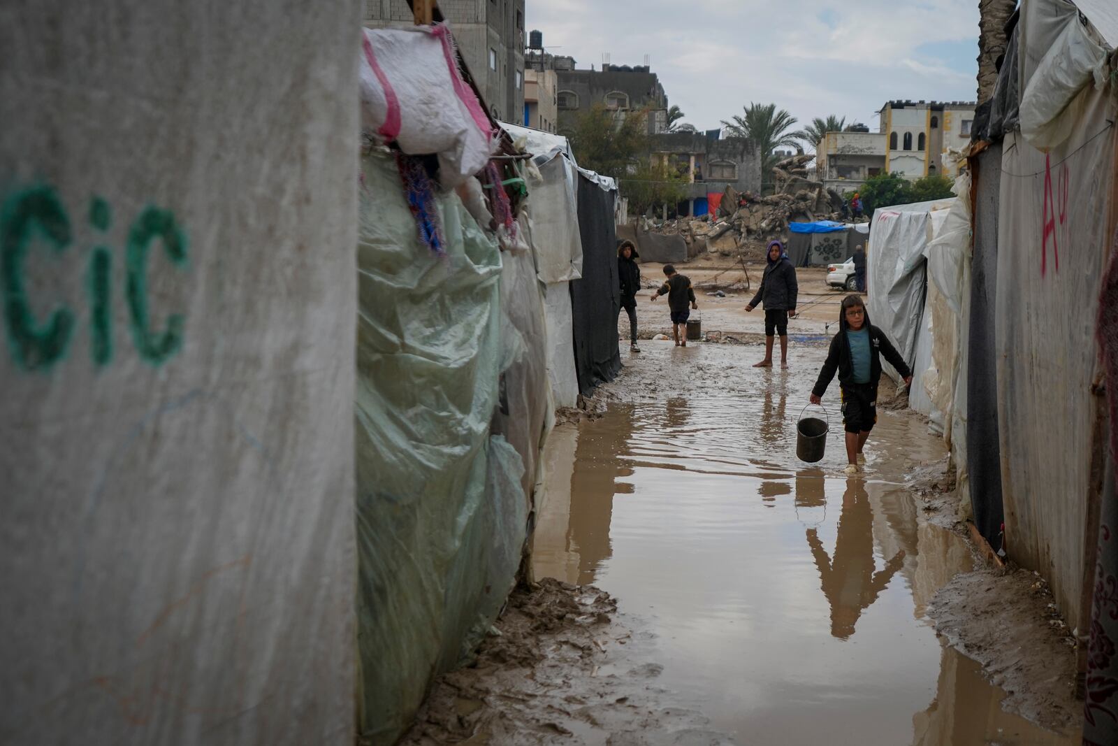 Palestinian children carry buckets of water after overnight rainfall at the refugee tent camp for displaced Palestinians in Deir al-Balah, central Gaza Strip, Tuesday, Dec. 31, 2024. (AP Photo/Abdel Kareem Hana)