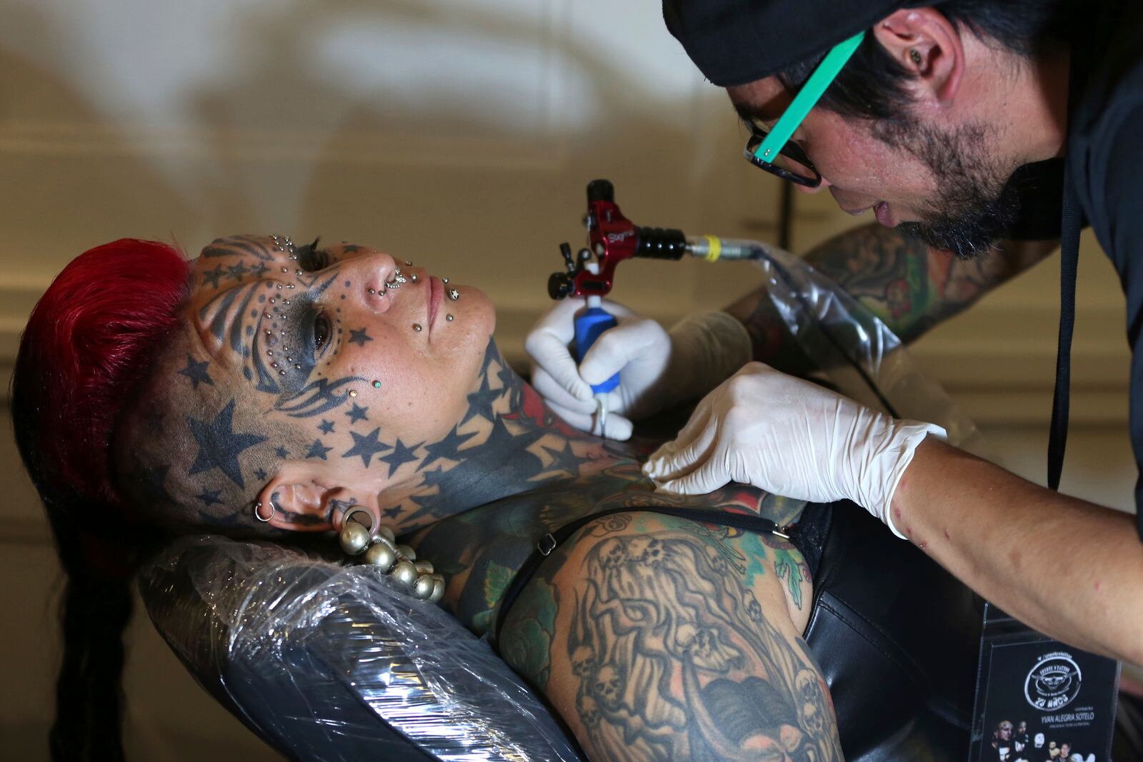 FILE - Gaby Peralta sits still as a tattoo artist draws a tattoo on her neck at a tattoo fair in Lima, Peru, Saturday, Sept. 6, 2014. (AP Photo/Martin Mejia, File)