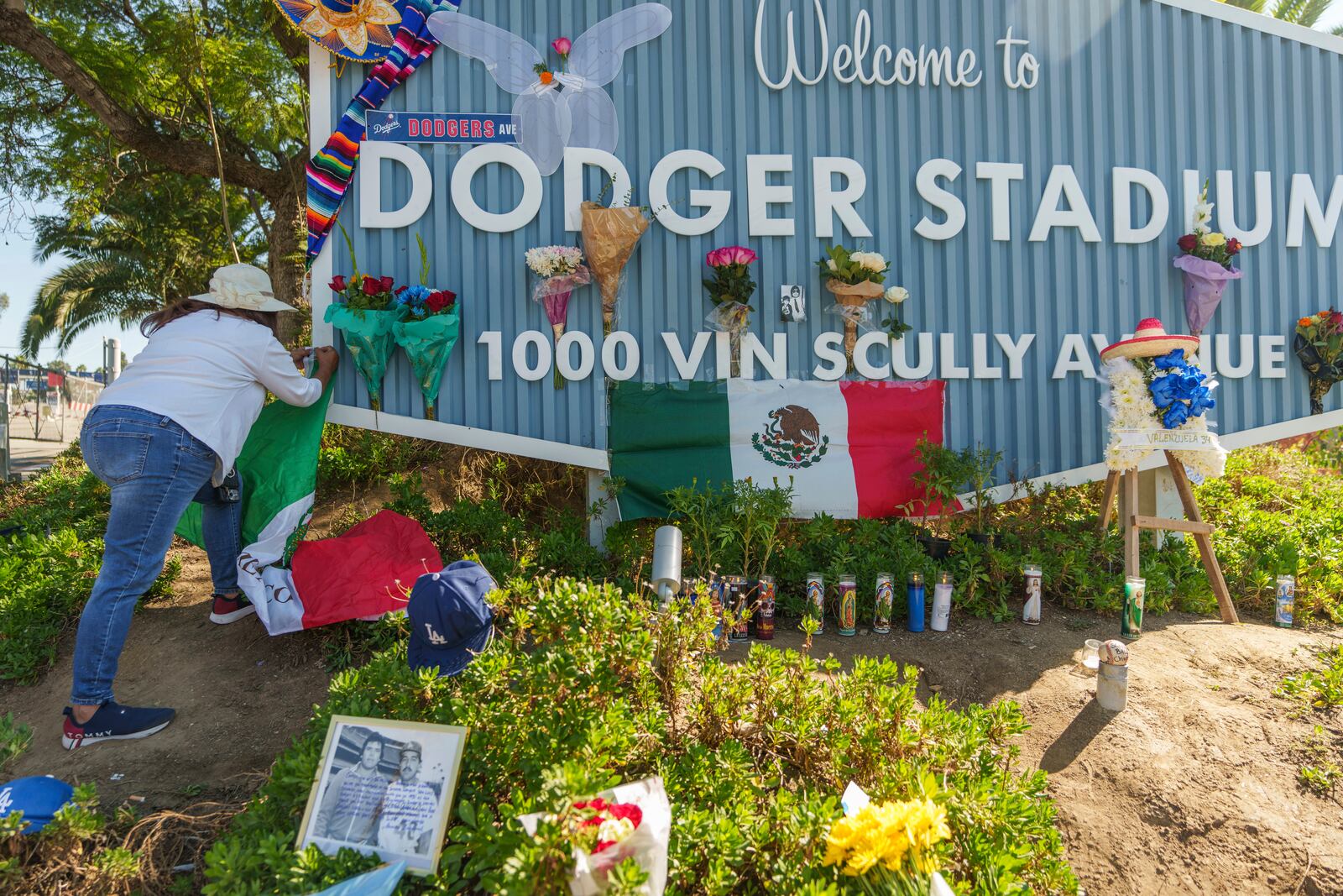 Cristina Vargas from North Hollywood, places a Mexican flag among baseball memorabilia, flowers, and candles placed outside Dodger Stadium after the death of former Dodgers pitcher Fernando Valenzuela Wednesday, Oct. 23, 2024, in Los Angeles. Valenzuela, the Mexican-born phenom for the Los Angeles Dodgers who inspired "Fernandomania" while winning the NL Cy Young Award and Rookie of the Year in 1981, died Tuesday, Oct. 22, 2024. (AP Photo/Damian Dovarganes)