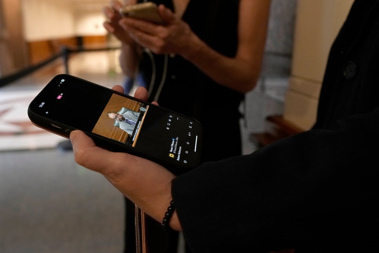 A person waiting outside a hearing room watches a live feed of the committee hearing as State Rep. Joe Moody, D-El Paso, makes comments Monday, Oct. 21, 2024, in Austin, Texas. (AP Photo/Tony Gutierrez)