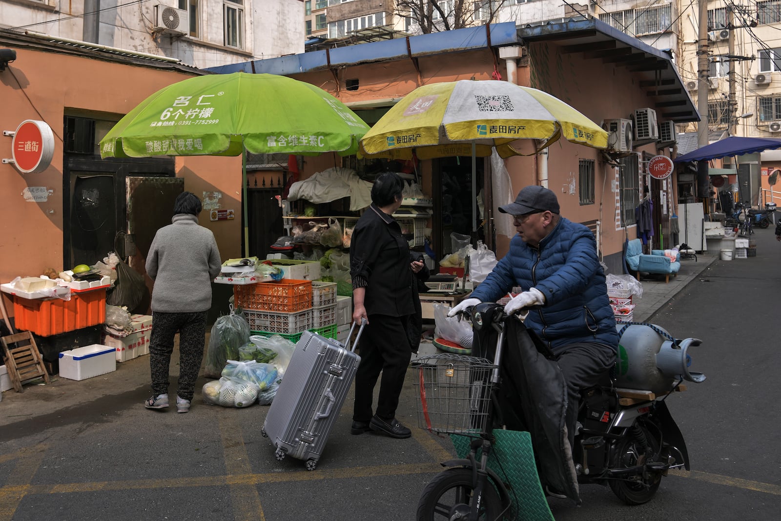 A vendor delivers a gas cylinder passes by residents at a market in Beijing, Sunday, March 9, 2025. (AP Photo/Andy Wong)