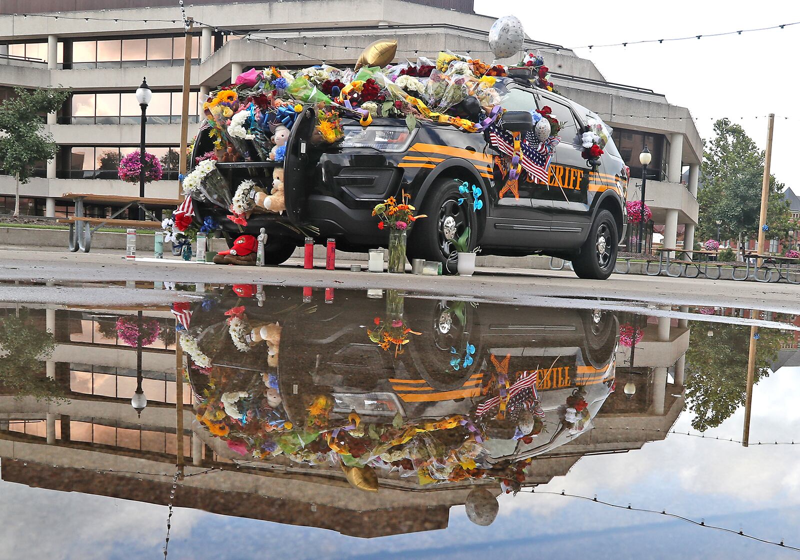 The Clark County Sheriff's vehicle that was set up as a memorial for Deputy Matthew Yates is reflected in a rain puddle on the Springfield City Hall Plaza Thursday, July 28, 2022. BILL LACKEY/STAFF