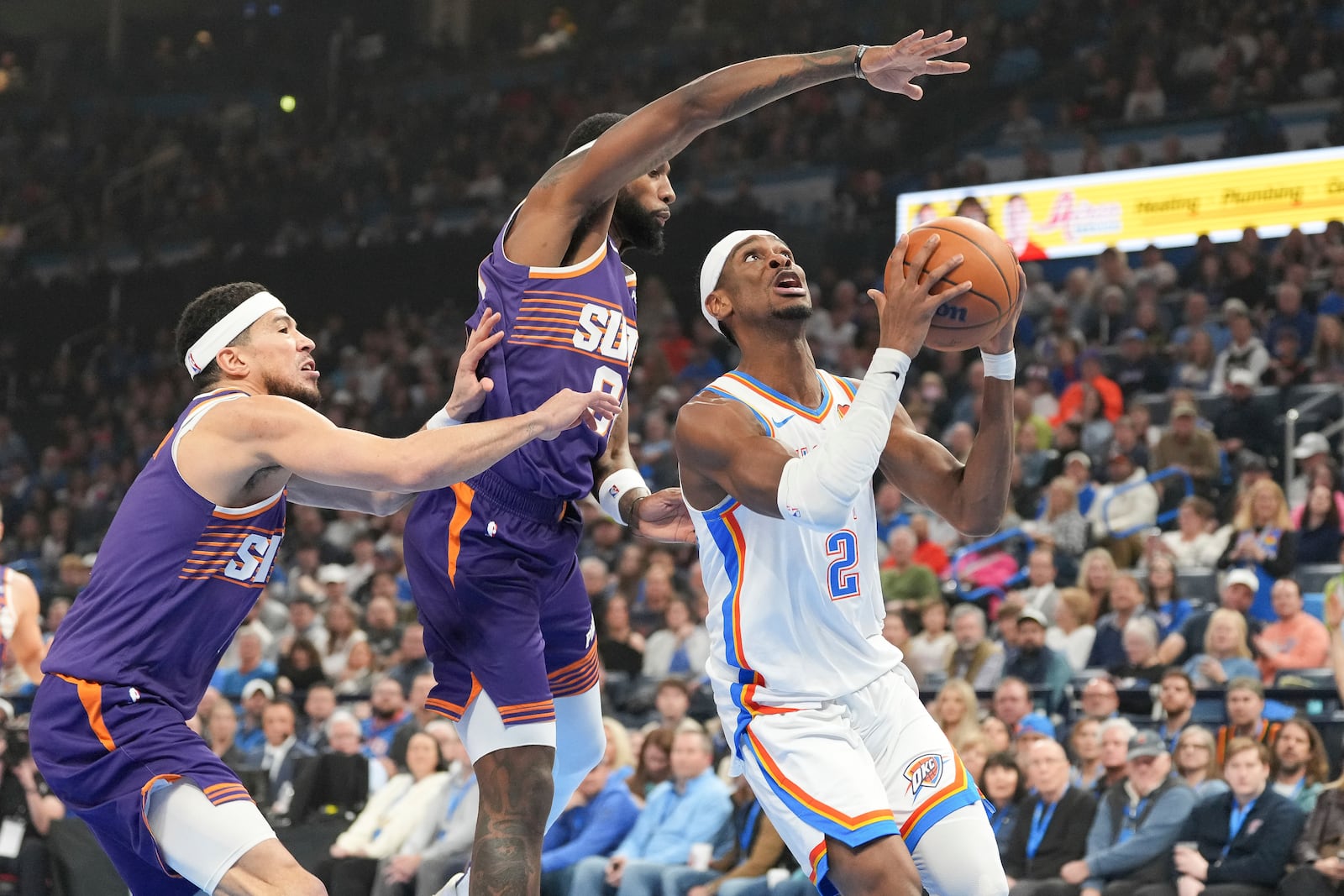 Oklahoma City Thunder guard Shai Gilgeous-Alexander, right, drives past Phoenix Suns forward Royce O'Neale, middle and guard Devin Booker, left, during the first half of an NBA basketball game, Wednesday, Feb. 5, 2025, in Oklahoma City. (AP Photo/Kyle Phillips)