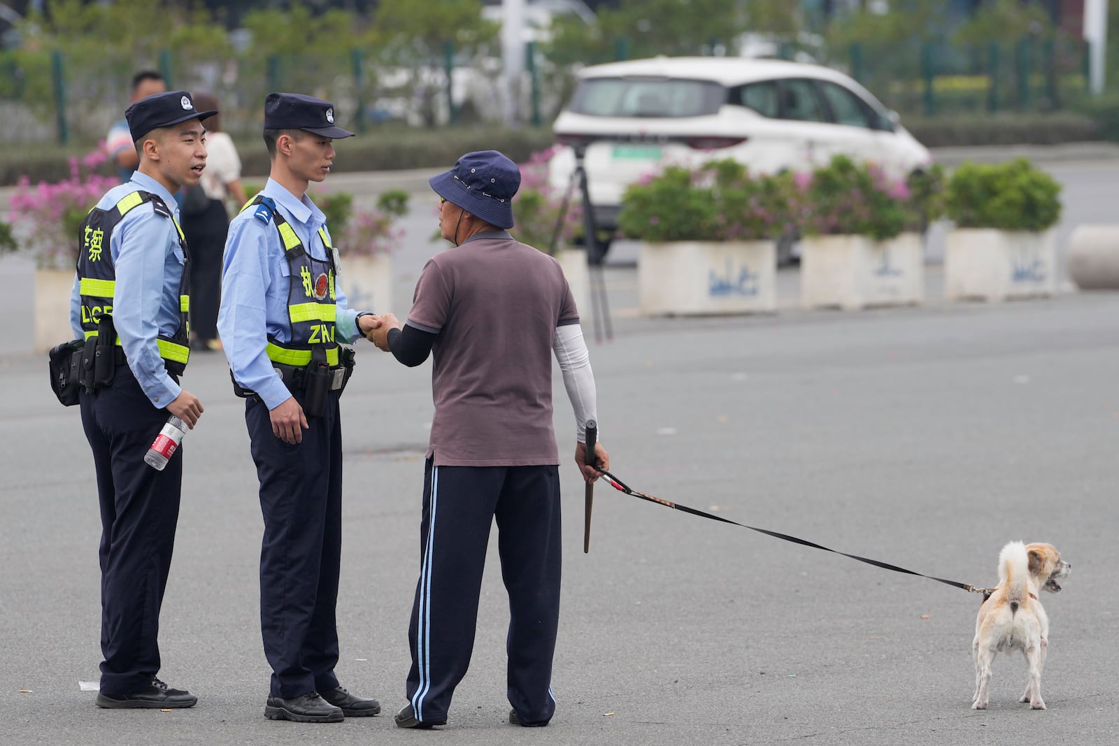 Police officers talk with a man walking his dog in front of the "Zhuhai People's Fitness Plaza" where a man deliberately rammed his car into people exercising at the sports center, killed some and injured others in Zhuhai, southern China's Guangdong province, Wednesday, Nov. 13, 2024. (AP Photo/Ng Han Guan)