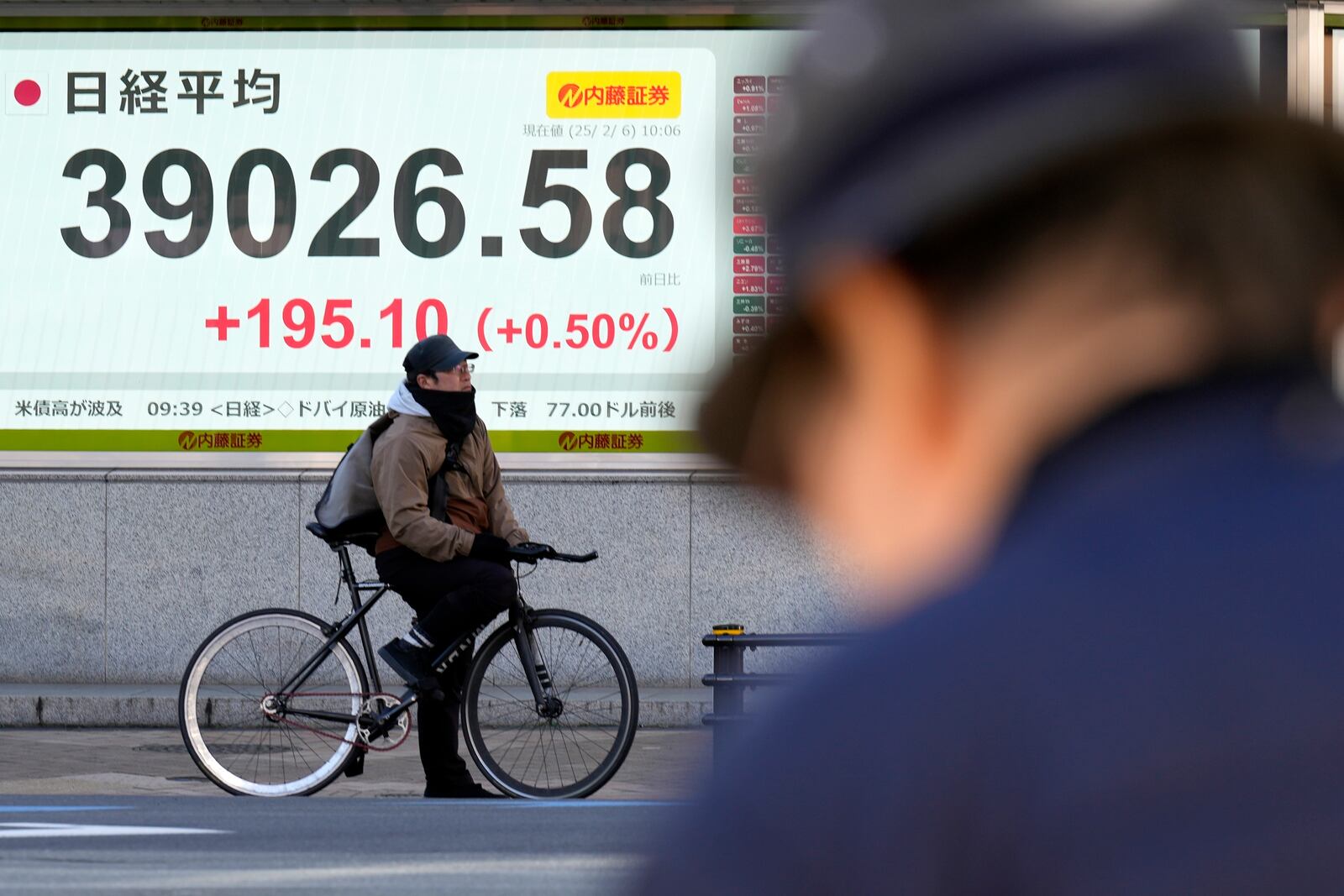 A person riding a bicycle waits in front of an electronic stock board showing Japan's Nikkei index at a securities firm Thursday, Feb. 6, 2025, in Tokyo. (AP Photo/Eugene Hoshiko)