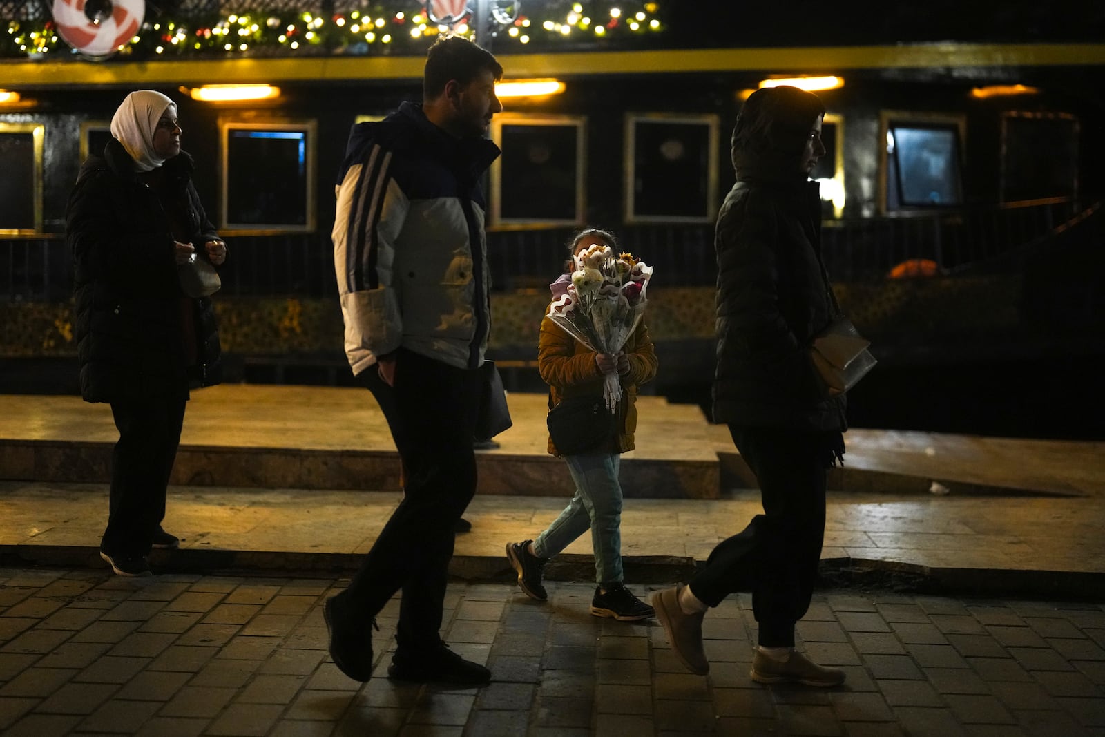 A girl sells flowers to passersby on the Karakoy sea promenade in Istanbul, Turkey, Friday, Dec. 6, 2024. (AP Photo/Francisco Seco)