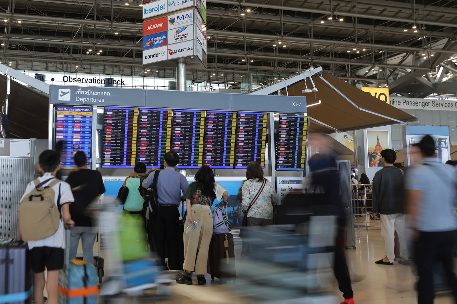 Tourists check an electronic board departure schedule at Suvarnabhumi International Airport in Samut Prakarn Province, Thailand, Sunday, Dec. 29, 2024. (AP Photo/Chatkla Samnaingjam)