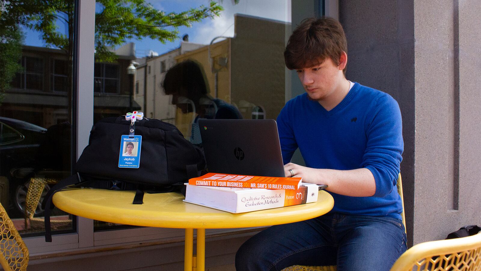 This photo illustration from Walmart shows an employee sitting outside at a table studying on a laptop. The company has expanded its education benefits program to high school students.