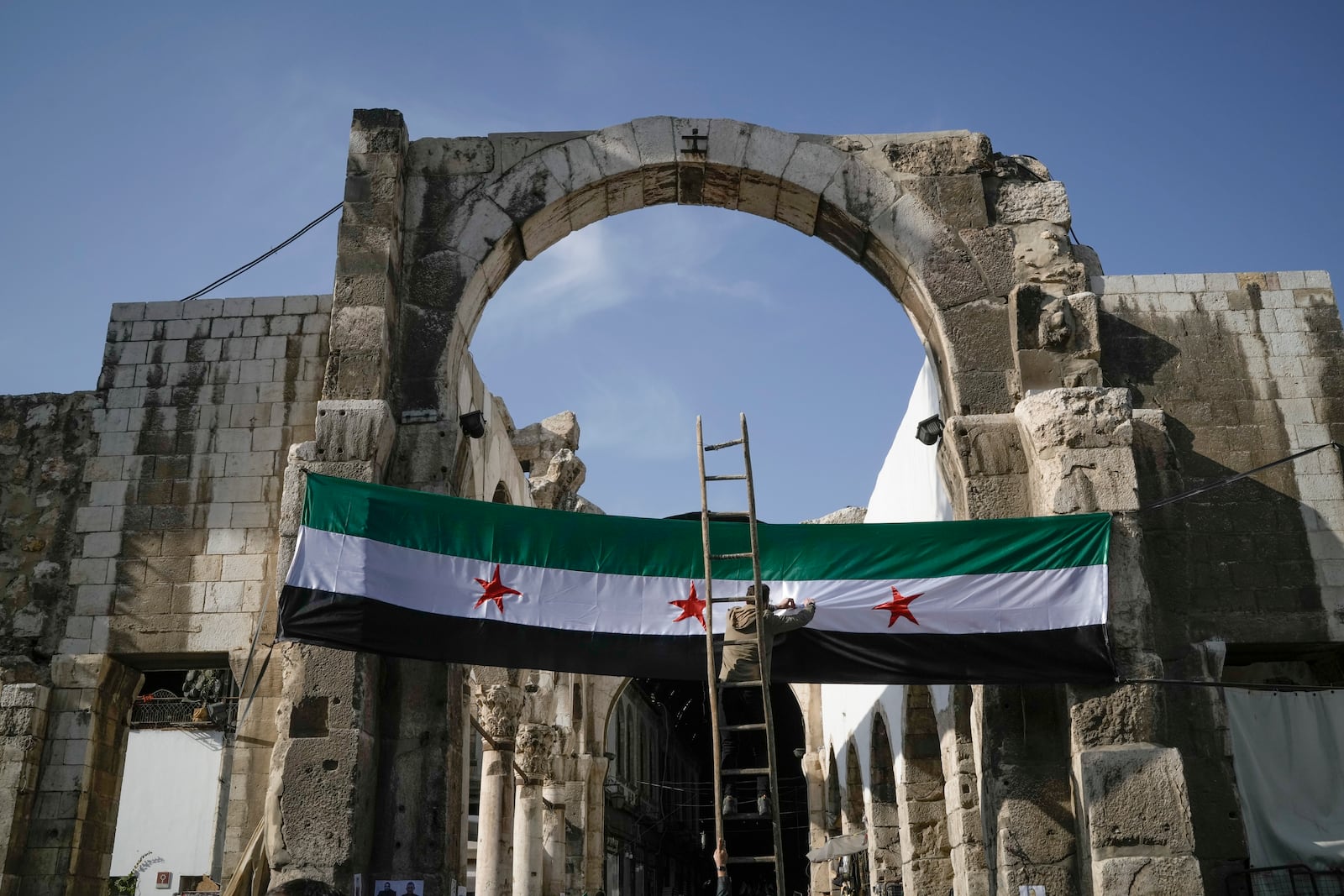 A worker sets up a Syrian "revolutionary" flag at the entrance of the Umayyad Mosque ahead of Friday prayers in Damascus, Syria, Friday Dec. 20, 2024. 2024.(AP Photo/Leo Correa)