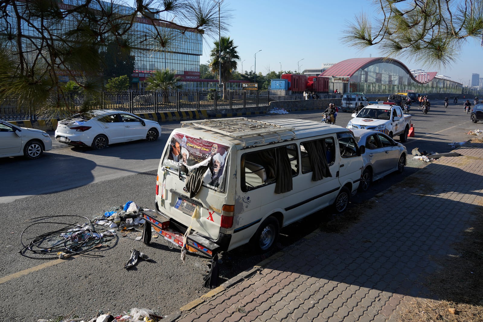 A motorcyclist drives through the damaged vehicles left behind by supporters of imprisoned former Prime Minister Imran Khan's Pakistan Tehreek-e-Insaf party when security forces launched an operation Tuesday night to disperse them, in Islamabad, Pakistan, Wednesday, Nov. 27, 2024. (AP Photo/Anjum Naveed)