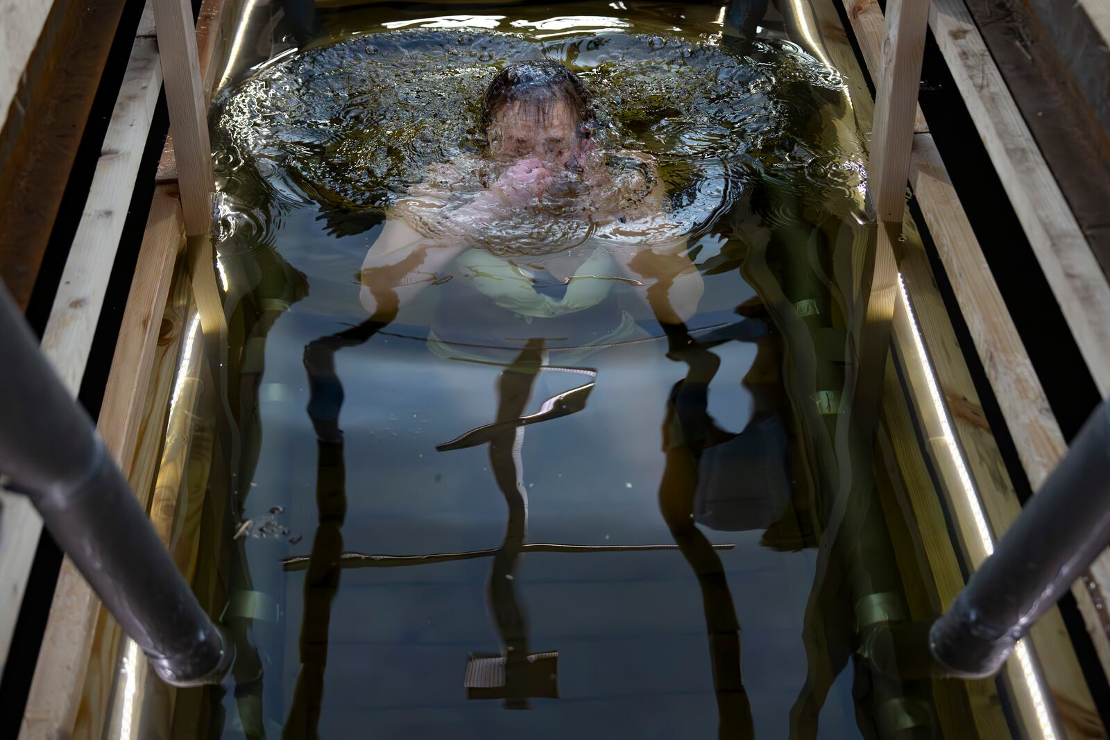 A woman plunge as a cross is reflected in icy water celebrating the Orthodox Epiphany in the Stroginskaya floodplain in Moscow, Russia, on Sunday, Jan. 19, 2025. (AP Photo/Alexander Zemlianichenko)