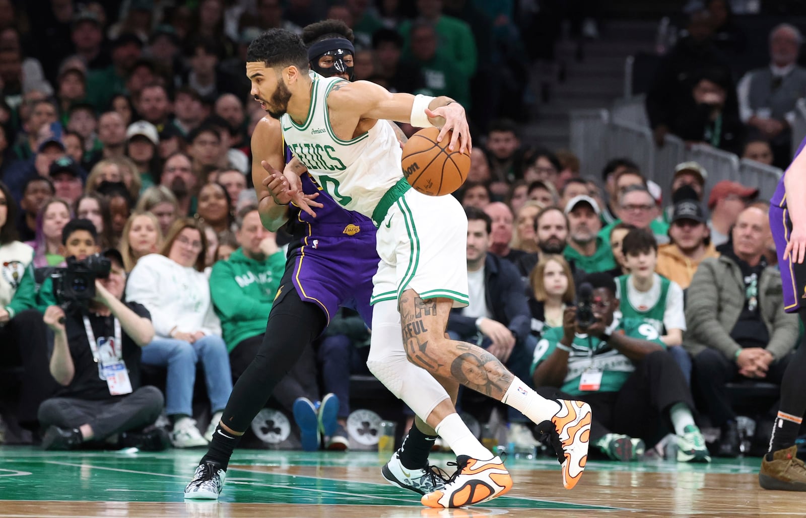 Boston Celtics forward Jayson Tatum (0) dribbles the ball around Los Angeles Lakers guard Jordan Goodwin during the first half of an NBA basketball game, Saturday, March 8, 2025, in Boston. (AP Photo/Mark Stockwell)