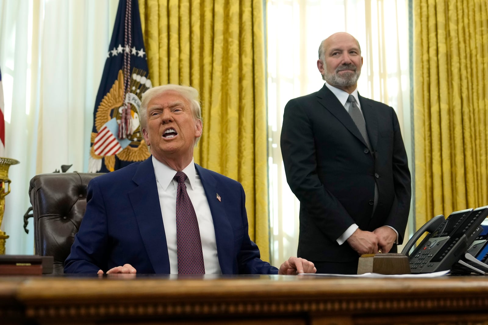 President Donald Trump speaks to reporters as Commerce Secretary nominee Howard Lutnick listens after Trump signed an executive order in the Oval Office of the White House, Thursday, Feb. 13, 2025, in Washington. (AP Photo/Ben Curtis)