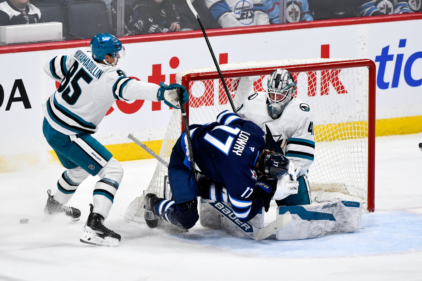 Winnipeg Jets' Adam Lowry (17) collides with San Jose Sharks goaltender Vitek Vanecek after being checked by Shakir Mukhamadullin during the first period of an NHL hockey game in Winnipeg, Manitoba, Monday, Feb. 24, 2025. (Fred Greenslade/The Canadian Press via AP)