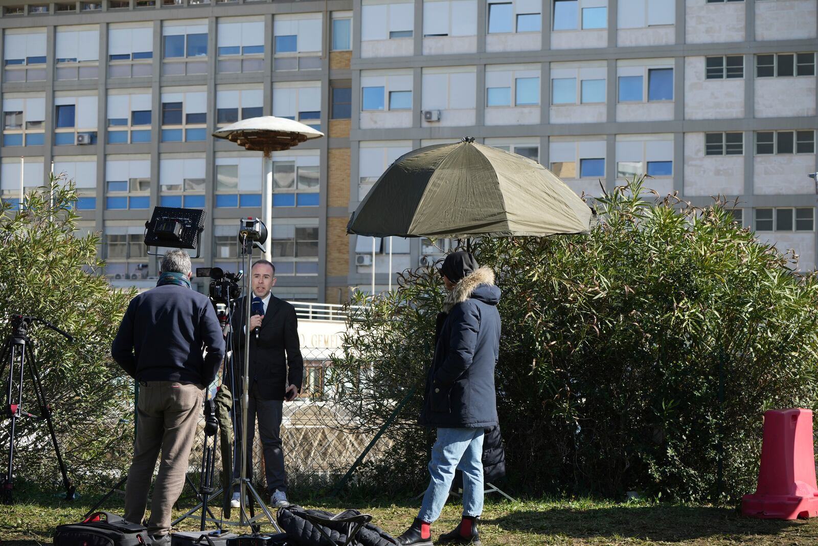 Journalists report from outside the Agostino Gemelli Polyclinic in Rome, Sunday, Feb. 16, 2025, where Pope Francis was hospitalised Friday after a weeklong bout of bronchitis worsened and is receiving drug therapy for a respiratory tract infection that made impossible for him to attend the traditional Sunday public blessing after the noon Angelus prayer. (AP Photo/Alessandra Tarantino)