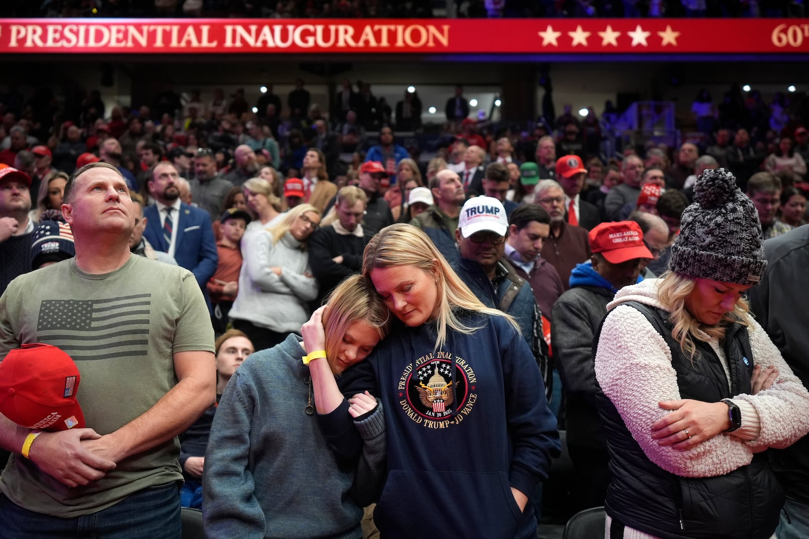 Supporters of President Donald Trump bow their heads during the invocation while watching inauguration ceremonies taking place at the U.S. Capitol on screens at Capitol One Arena in Washington, Monday, Jan. 20, 2025. (AP Photo/Mark Schiefelbein)