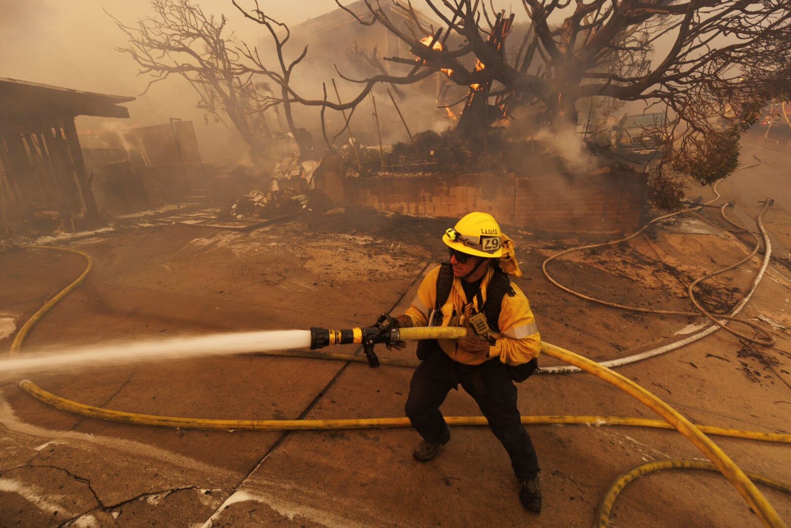 A firefighter hoses down flames from the Palisades Fire in front of a residence in the Pacific Palisades neighborhood of Los Angeles, Tuesday, Jan. 7, 2025. (AP Photo/Ethan Swope)