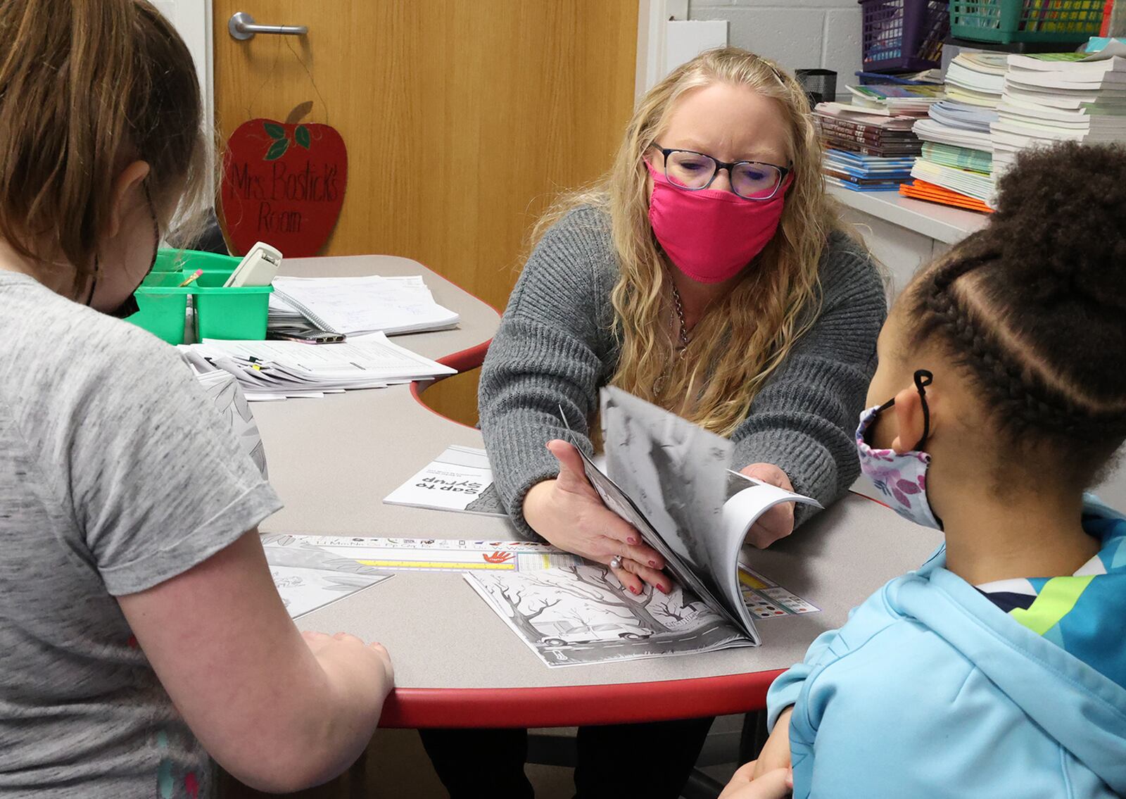 Beckitt Bostick, a second grade teacher at Perrin Woods Elementary, helps a student find the correct page in a work book Wednesday. BILL LACKEY/STAFF