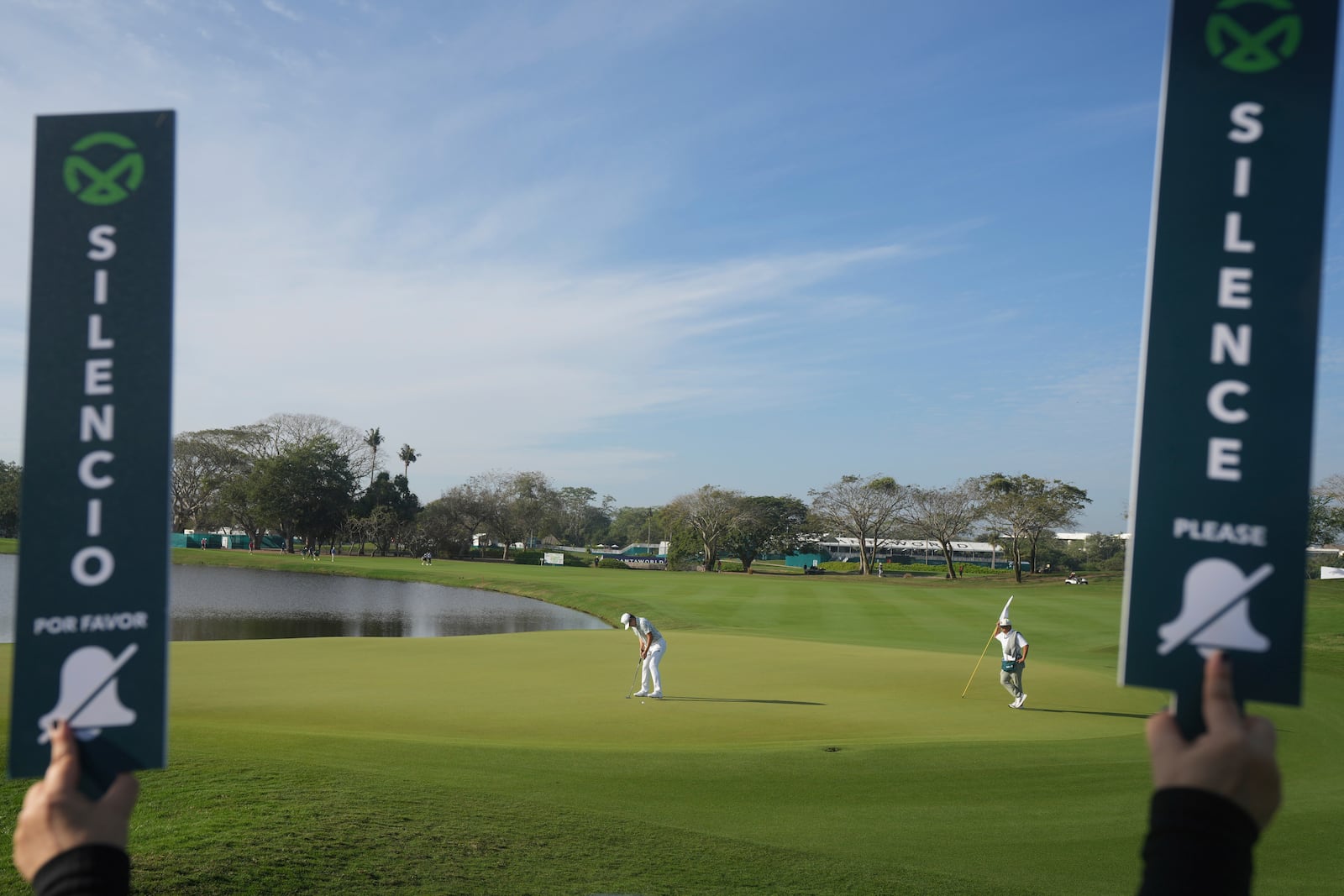 "Silence" signs are held up as Kaito Onishi, of Japan, watches his putt on the green of the first hole during the second round of the Mexico Open golf tournament in Puerto Vallarta, Mexico, Friday, Feb. 21, 2025. (AP Photo/Fernando Llano)