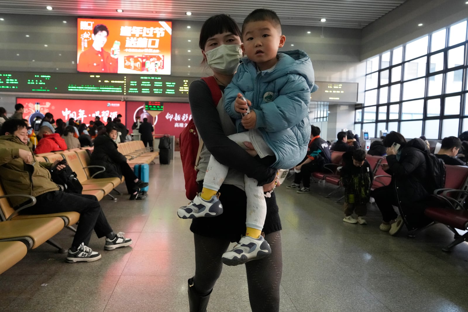 A woman carries a boy as they wait to board their train at the Beijing West Railway Station as families travel back home ahead of the Lunar New Year in Beijing on Friday, Jan. 24, 2025. (AP Photo/Aaron Favila)