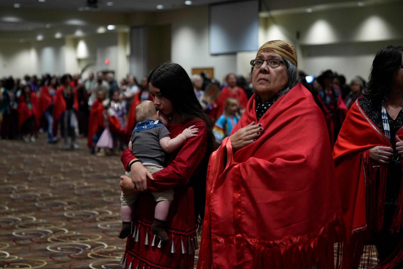 Confederated Tribes of Siletz Indians member Ramona Hudson, of Aumsville, Ore., right, looks up as her cousin Aurora Chulik-Ruff, 12, holds her five-month-old brother Bear Chulik-Moore, as they walk during a dance dedicated to missing and murdered indigenous women during a powwow at Chinook Winds Casino Resort, Saturday, Nov. 16, 2024, in Lincoln City, Ore. (AP Photo/Jenny Kane)