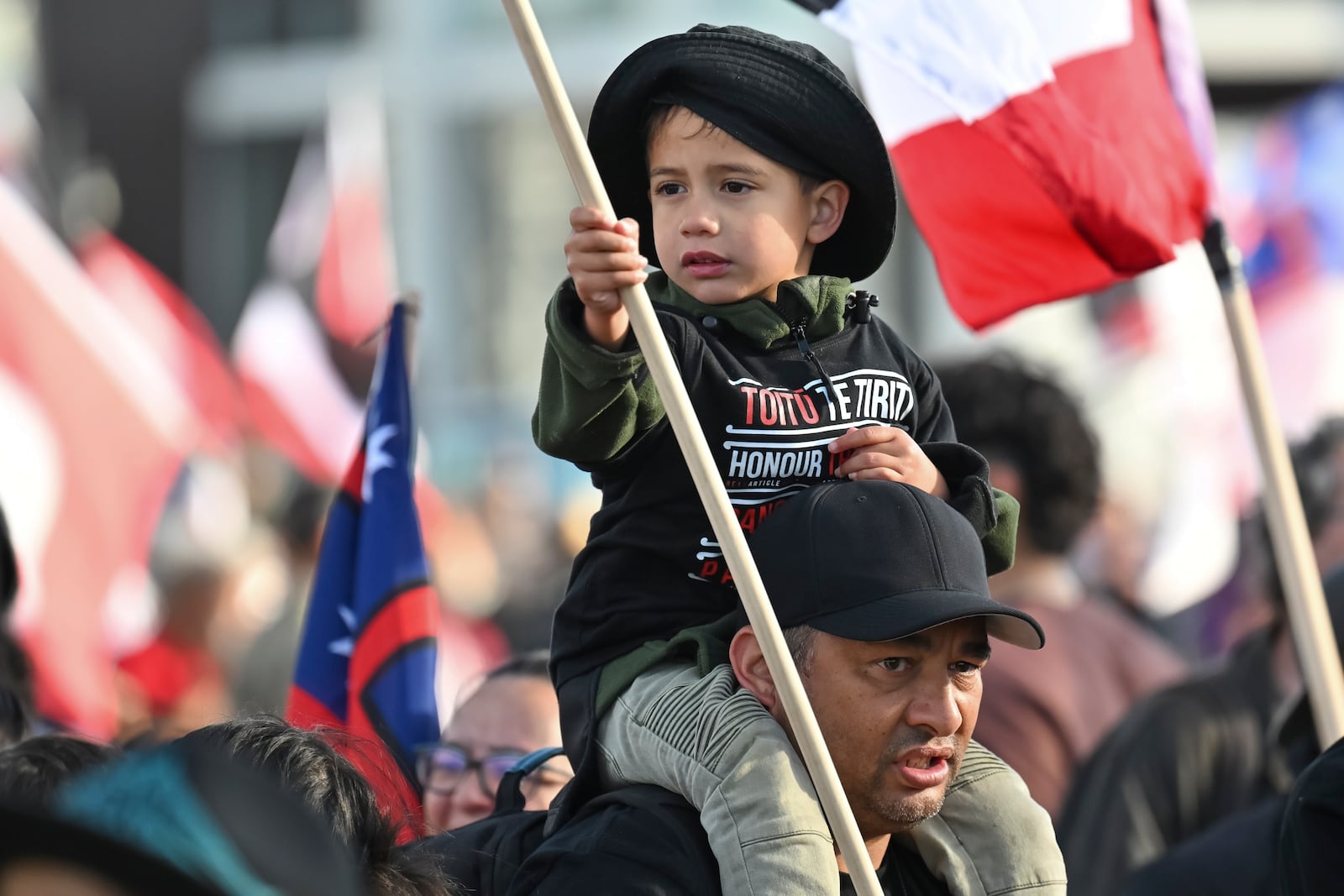 A man carries a child on his shoulders outside New Zealand's parliament during a protest against a proposed law that would redefine the country's founding agreement between Indigenous Māori and the British Crown, in Wellington Tuesday, Nov. 19, 2024. (AP Photo/Mark Tantrum)