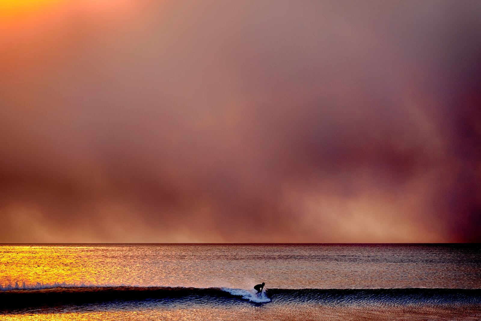 A surfer takes off on a wave in Santa Monica, Calif., during sunset under a blackened sky from the Palisades fire in the Pacific Palisades on Tuesday, Jan. 7, 2025. (AP Photo/Richard Vogel)