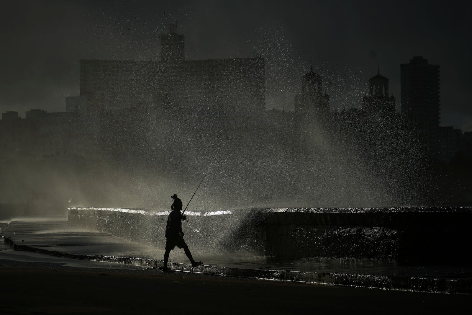 A person fishes along the boardwalk as waves break in Havana, Monday, Oct. 21, 2024. (AP Photo/Ramon Espinosa)