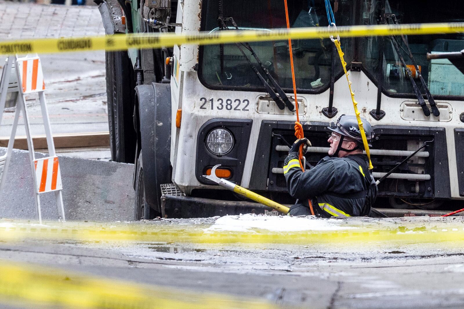 A hoist lowers an Omaha firefighter to attach a crane to a garbage truck that got stuck in a sinkhole in downtown Omaha, Neb., Thursday, Jan. 2, 2025. (Chris Machian/Omaha World-Herald via AP)