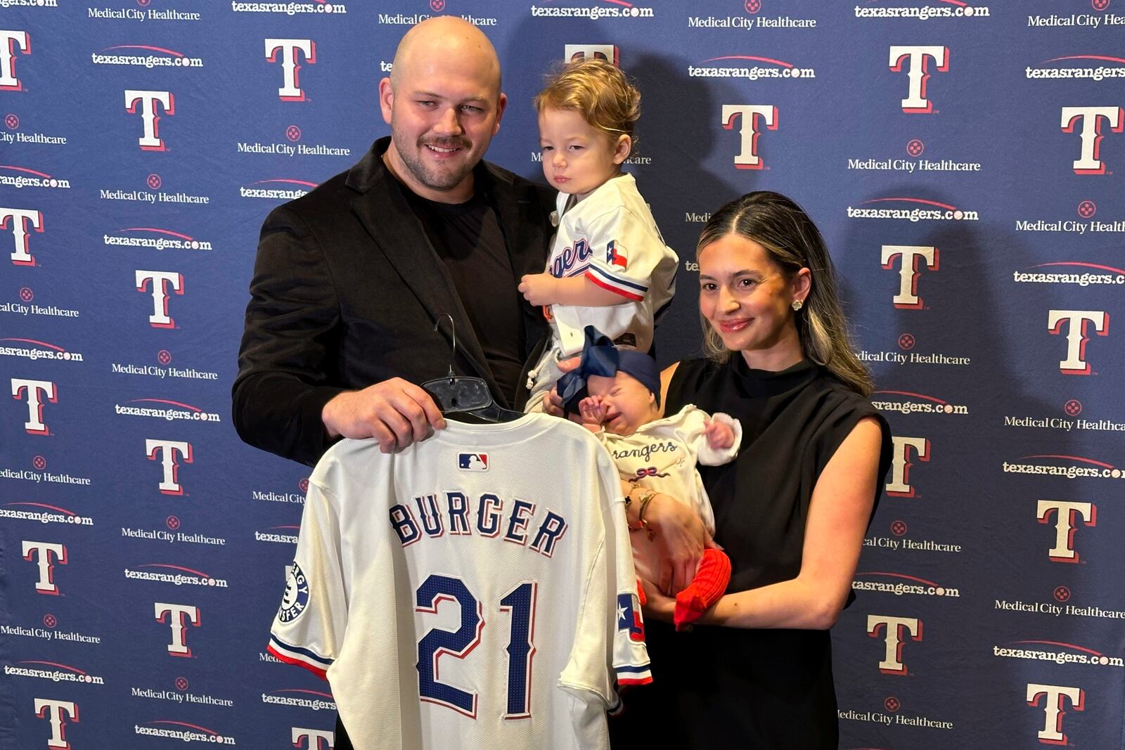 Texas Rangers first baseman Jake Burger poses at the team's awards dinner Friday, Jan. 17, 2025, in Arlington, Texas, with wife Ashyln, son Brooks and daughter Penelope while holding the No. 21 jersey that has special significance after his daughter was born with Down syndrome. (AP Photo/Stephen Hawkins)