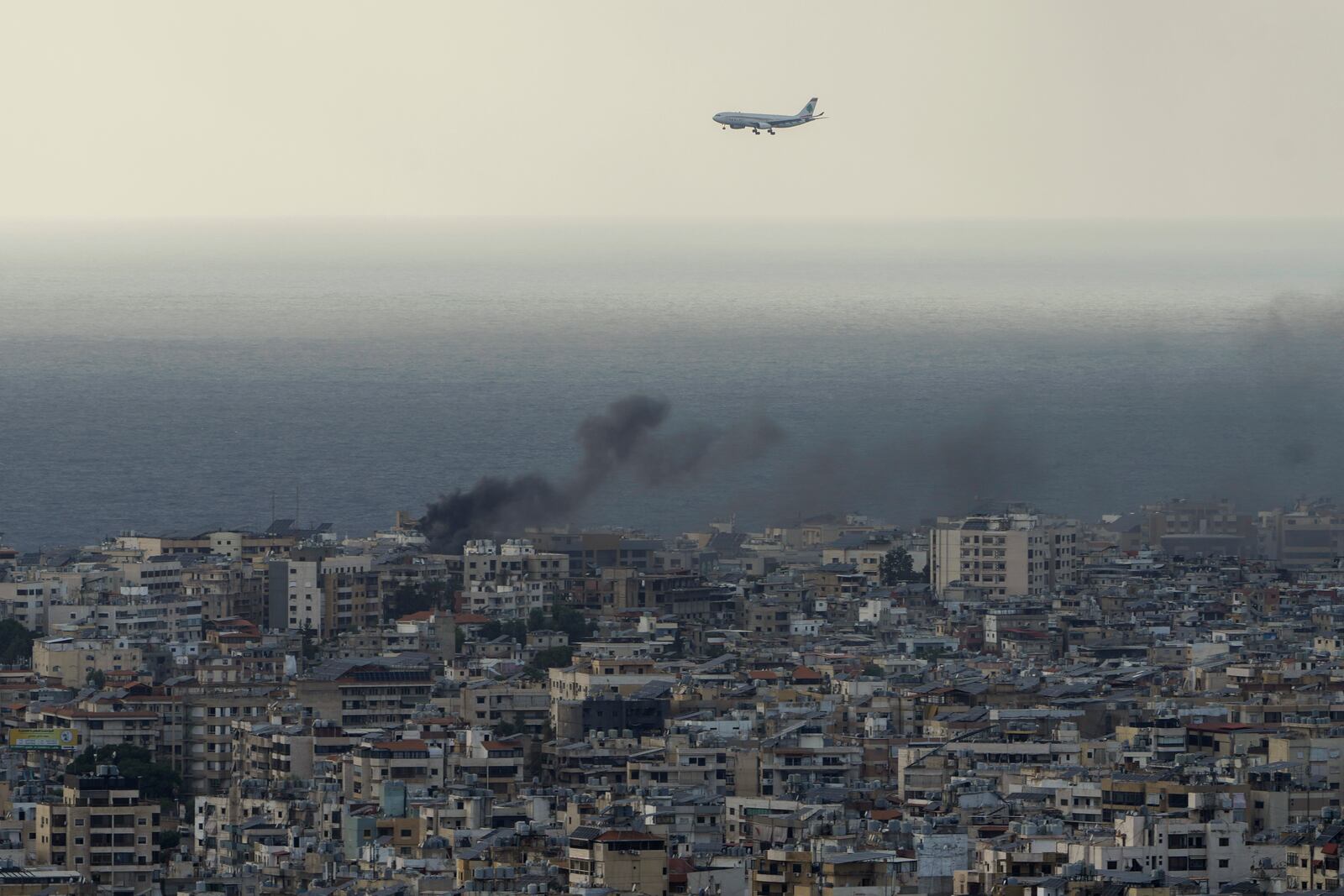 A Middle East Airlines airplane flies over Beirut as smoke rises from Israeli airstrikes in Dahiyeh, Beirut, Tuesday, Oct. 1, 2024. (AP Photo/Bilal Hussein)