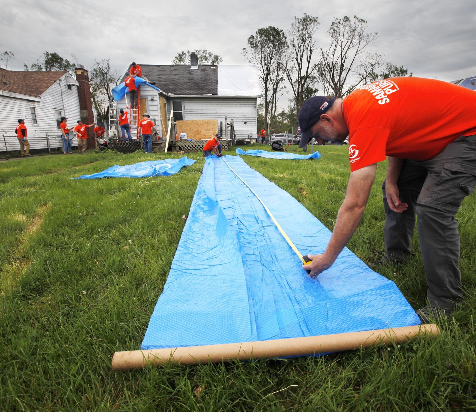 Volunteers with Samaritan’s Purse worked in this Harrison Twp. neighborhood and others that were affected by tornado damage. Andrew Jordan, right, measures a blue tarp for the roof of this house on Maumee Avenue. TY GREENLEES / STAFF