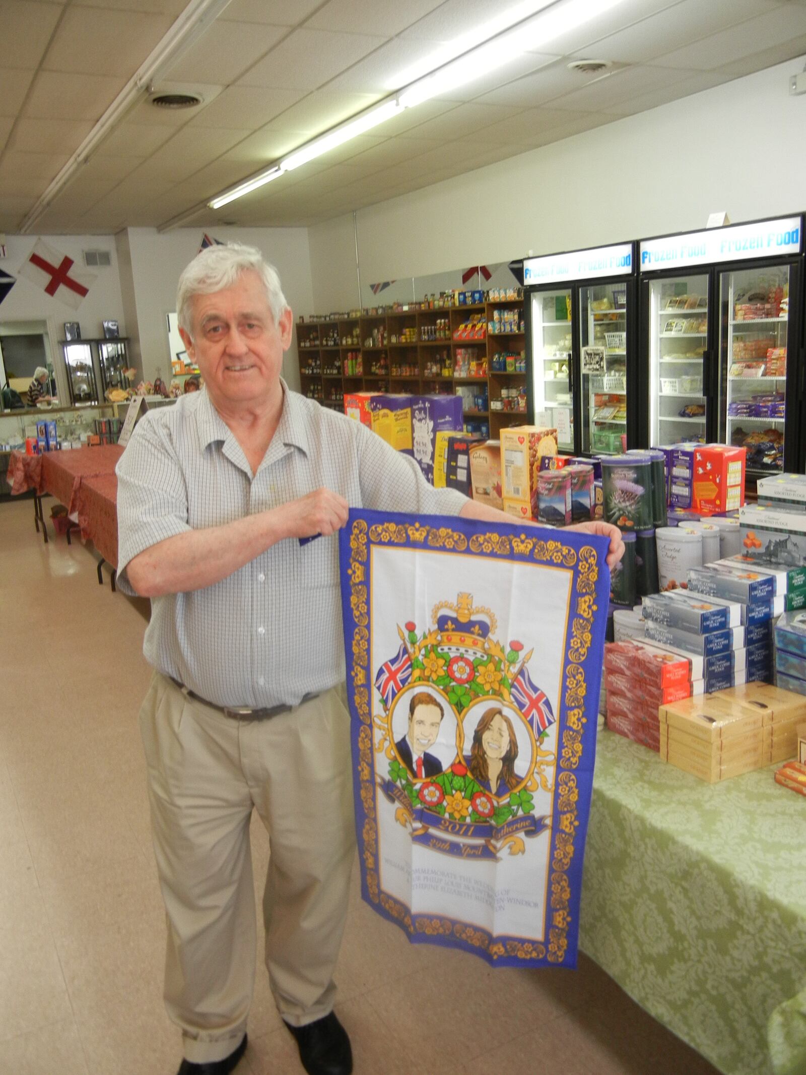 Harry Caswell, owner of Wise Choice British Foods, Gifts and Candies in Huber Heights, holds of a wall hanging featuring a image of Prince William and Kate Middleton.  staff photo by Amelia Robinson