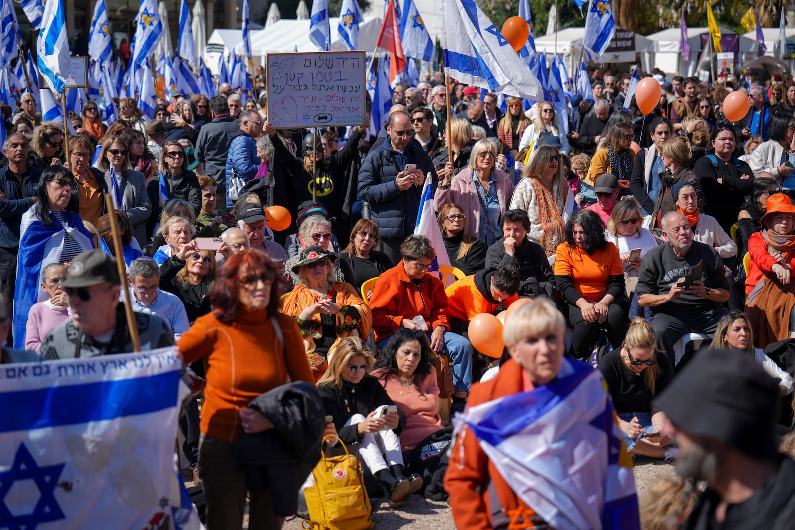 People watch a live broadcast from the funeral of slain hostages Shiri Bibas and her two children, Ariel and Kfir, at a plaza known as the Hostages Square in Tel Aviv, Israel, Wednesday, Feb. 26, 2025. The mother and her two children were abducted by Hamas on Oct. 7, 2023, and their remains were returned from Gaza to Israel last week as part of a ceasefire agreement with Hamas. (AP Photo/Ariel Schalit)